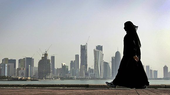 Una mujer camina frente a los rascacielos de Doha Qatar.