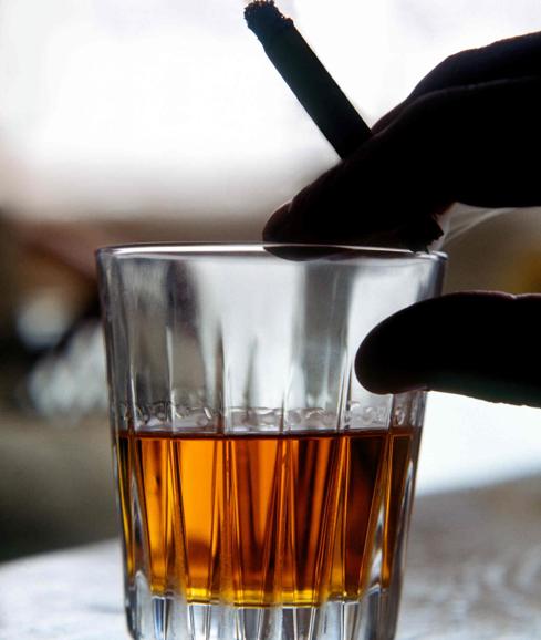 Un hombre toma un vaso de whisky mientras fuma un cigarrillo